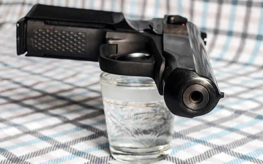 A gun laying on top of a short glass