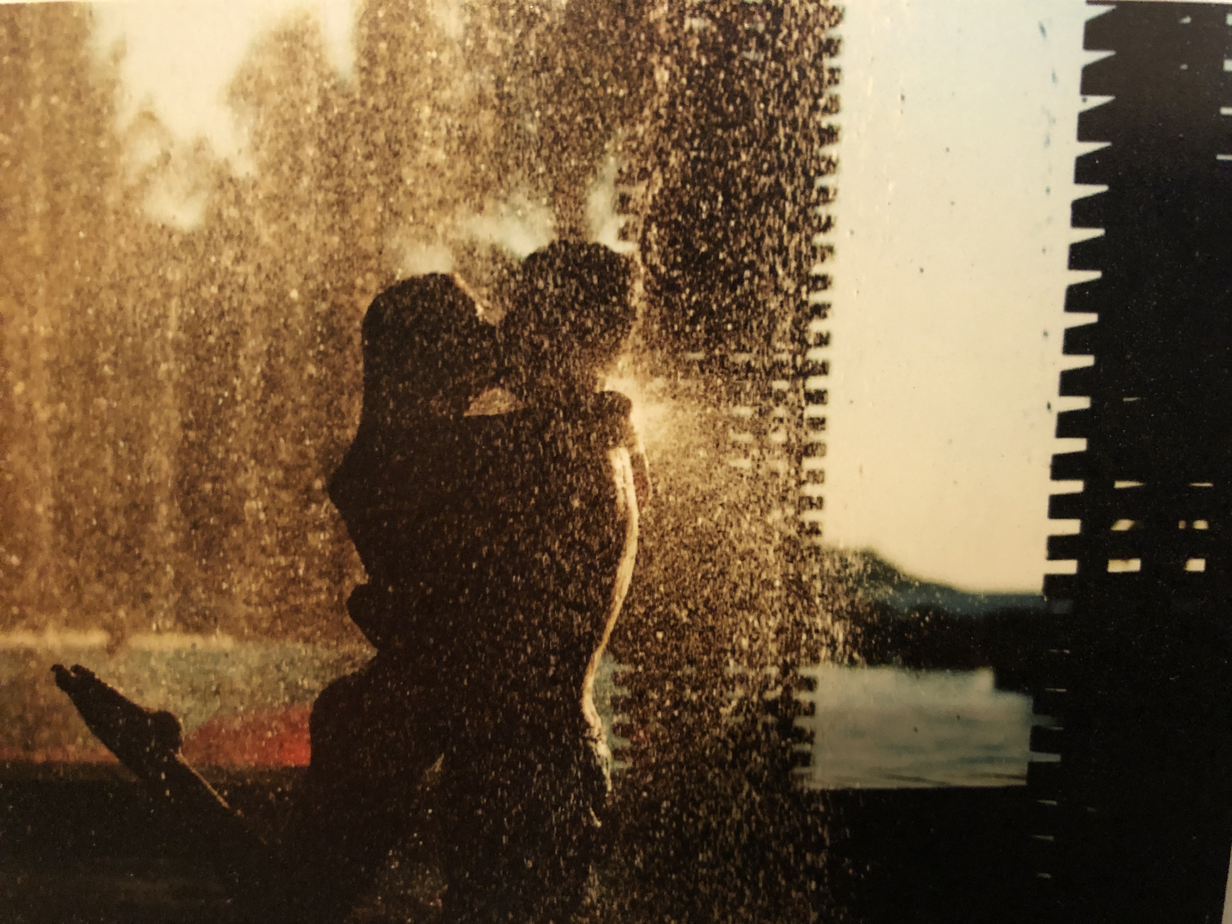 A silhouetted couple kisses while standing in the rain